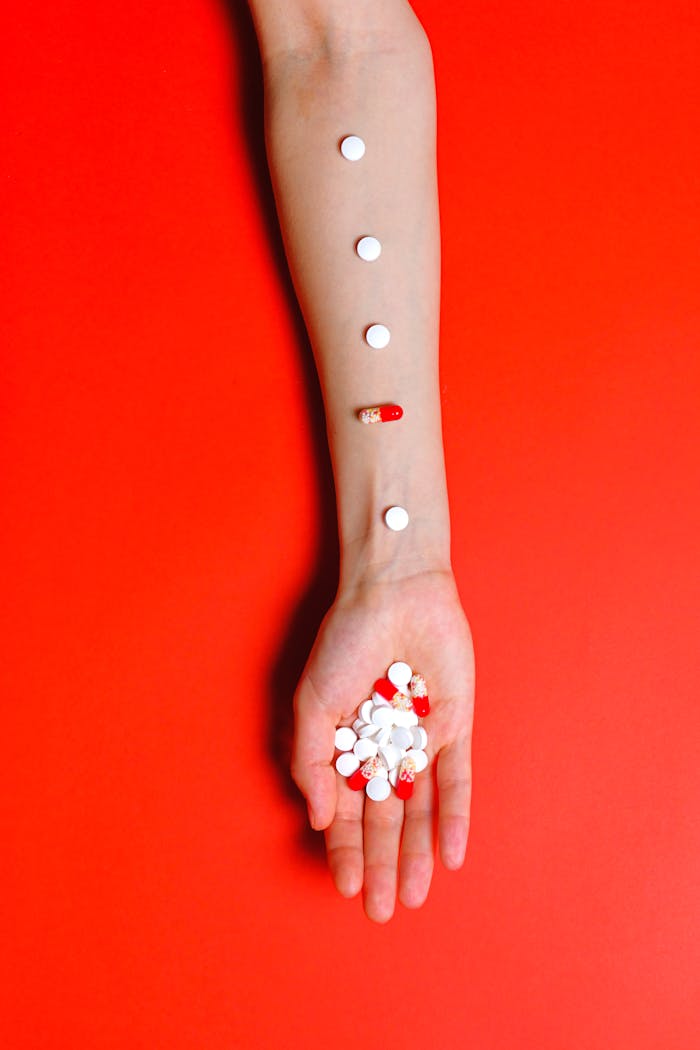 Artistic arrangement of pills on an arm with bold red background symbolizes healthcare concepts.